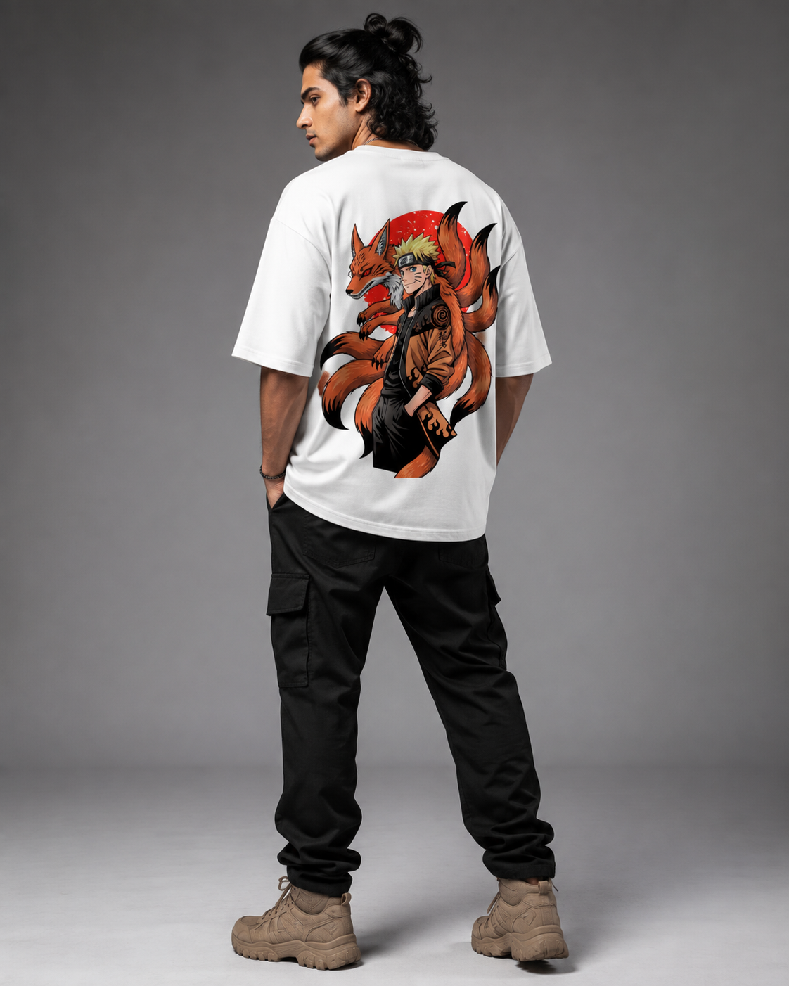 A man shown from the back wearing a white t-shirt with a large graphic of Naruto and his fox companion on the back, paired with black cargo pants and tan boots, against a gray studio background.