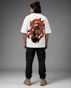 A man viewed from the back wearing a white oversized T-shirt with a large anime-style graphic on the back, paired with black cargo pants and tan boots, against a gray studio background.