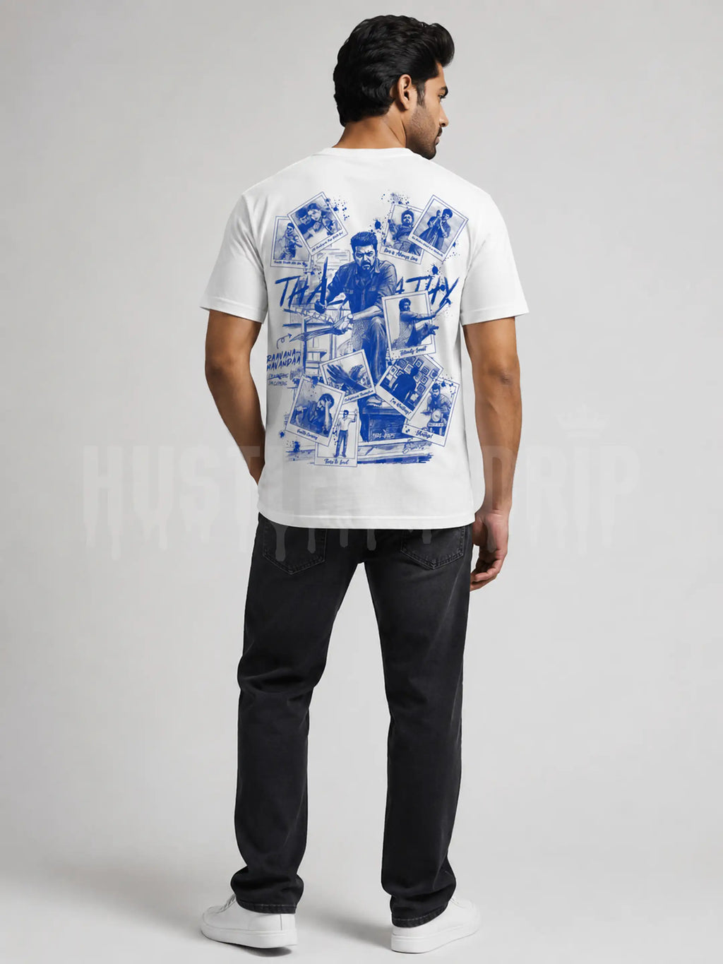 A man shown from the back wearing a white t-shirt with a large blue graphic print on the back, paired with black jeans and white sneakers, against a light gray studio background.