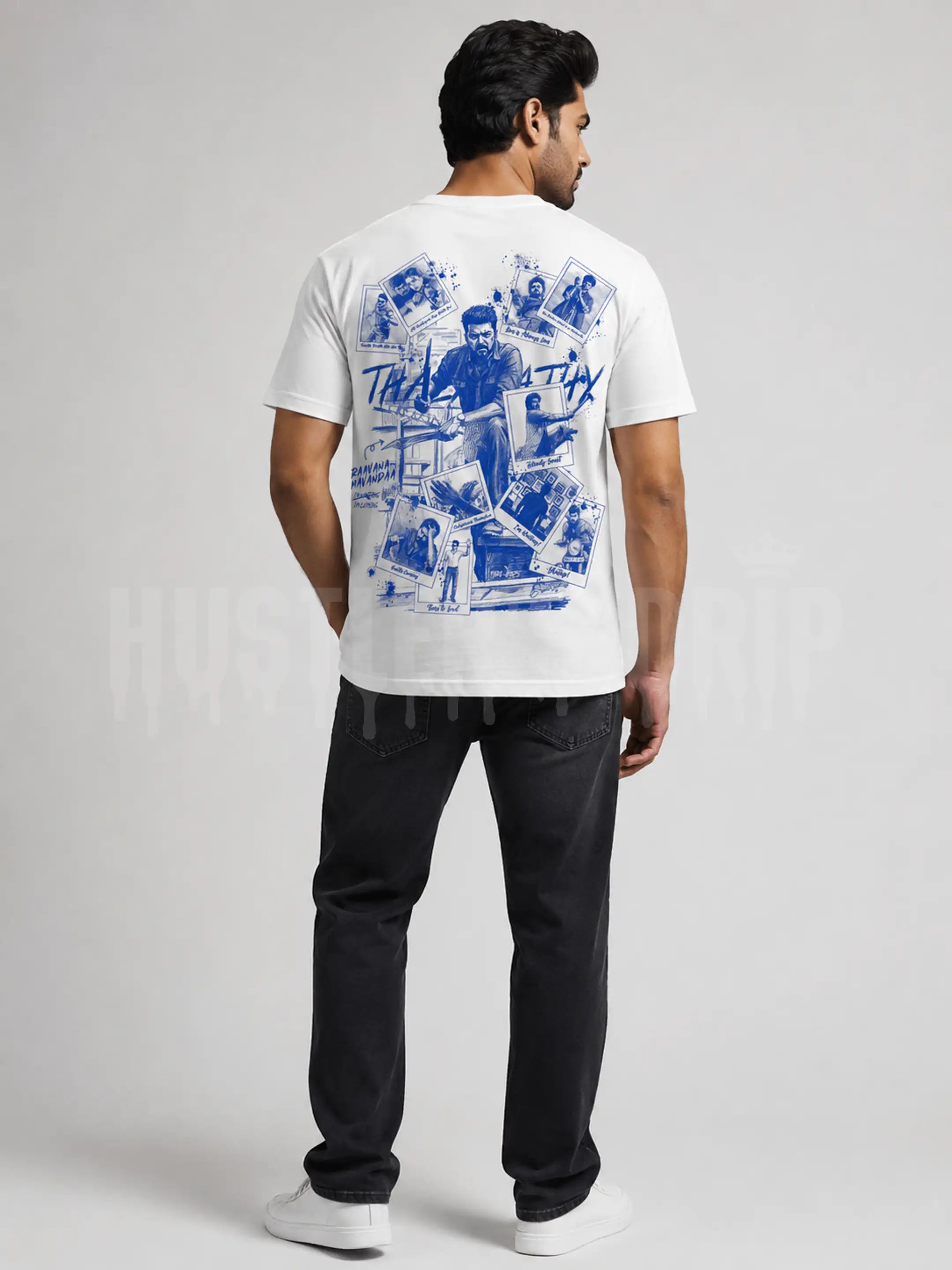 A man shown from the back wearing a white t-shirt with a large blue graphic print on the back, paired with black jeans and white sneakers, against a light gray studio background.