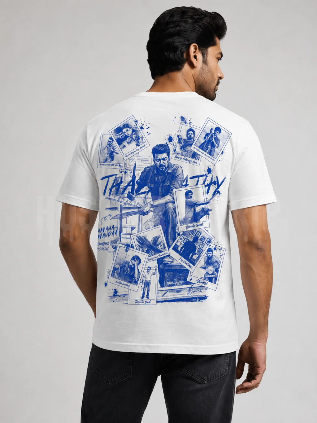 A man shown from the back wearing a white t-shirt with a large blue graphic collage print on the back, paired with black jeans, against a light gray studio background.
