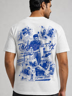 A man wearing a white t-shirt, viewed from the back. The shirt features a large blue graphic print on the back depicting a collage of action movie scenes and text, including 'THALAKATIX' and 'RAHUL MANGAL'.
