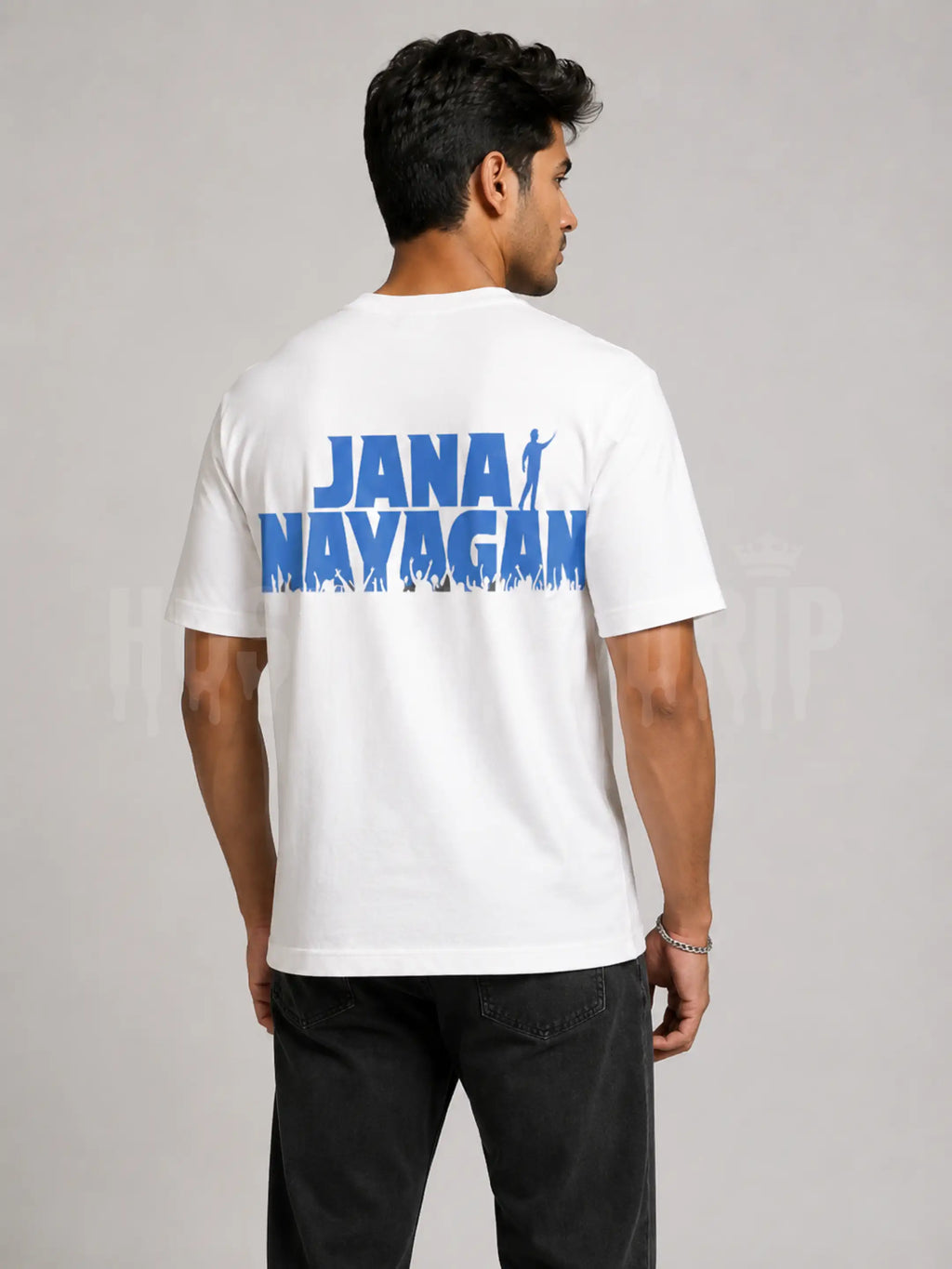 A man wearing a white t-shirt with a bold blue graphic print reading 'JANA NAYAGAN' on the back, shown from behind against a neutral gray studio background.