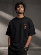 Man wearing a Suriya Karuppu black t-shirt with a graphic design against a gray background