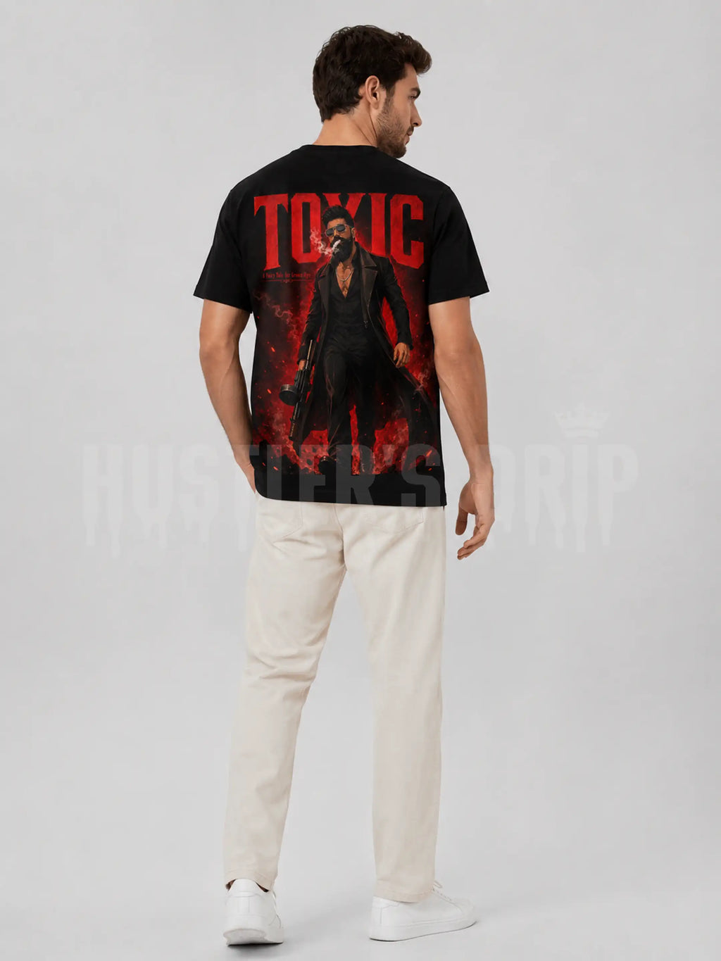 A man wearing a black graphic t-shirt with a large red and black print on the back, paired with off-white trousers and white sneakers, shown from a rear three-quarter view against a light gray studio background.