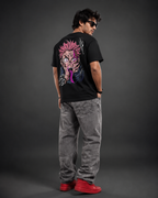 A man wearing a black graphic t-shirt with a large anime character print on the back, paired with gray jeans and red sneakers, photographed from behind against a dark gray studio background.