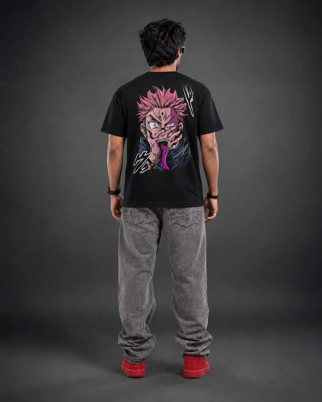 A person shown from the back wearing a black graphic T-shirt with a large anime-style character print in pink, purple, and white, paired with gray jeans and red shoes, against a dark gray studio background.