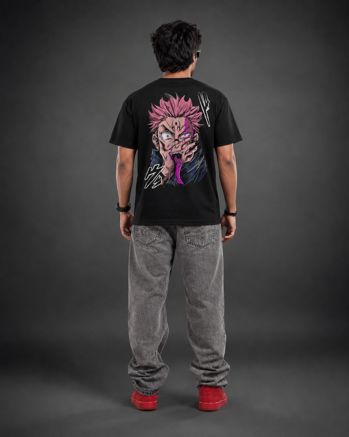 A person shown from the back wearing a black graphic T-shirt with a large anime-style character print in pink, purple, and white, paired with gray jeans and red shoes, against a dark gray studio background.